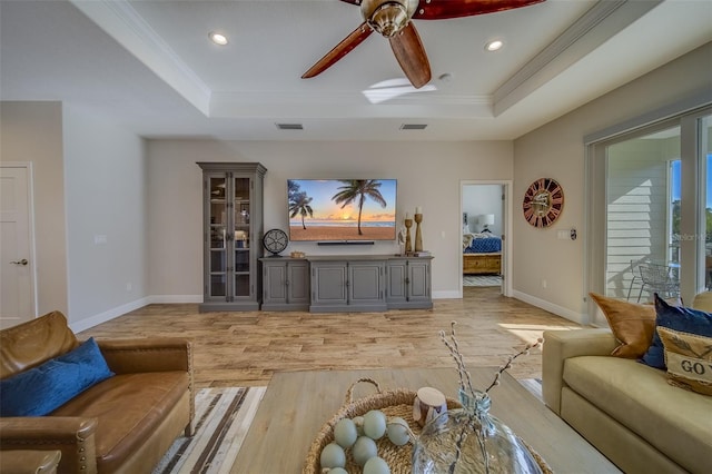 living room featuring a raised ceiling, ceiling fan, light wood-type flooring, and crown molding