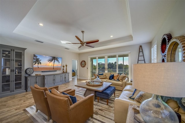 living room featuring a raised ceiling, ceiling fan, and light hardwood / wood-style flooring