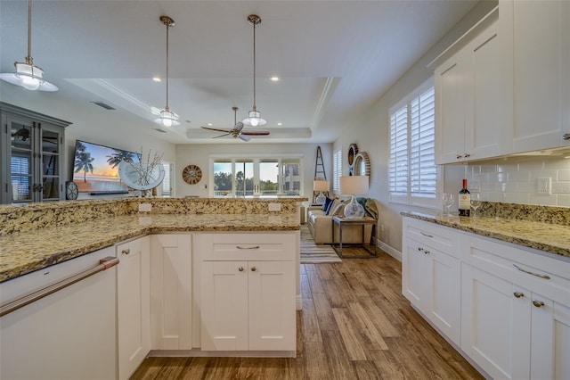 kitchen featuring hardwood / wood-style flooring, light stone countertops, pendant lighting, tasteful backsplash, and a tray ceiling