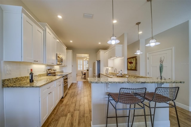 kitchen with stainless steel appliances, light wood-type flooring, hanging light fixtures, white cabinets, and sink