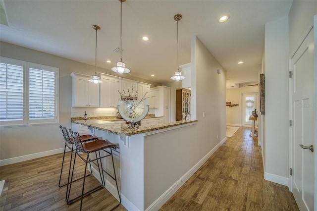 kitchen featuring a breakfast bar area, hanging light fixtures, light stone countertops, kitchen peninsula, and white cabinets