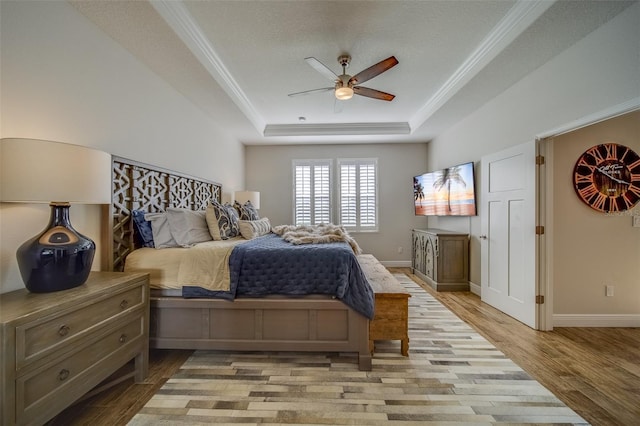 bedroom featuring a textured ceiling, light hardwood / wood-style flooring, ceiling fan, a tray ceiling, and ornamental molding