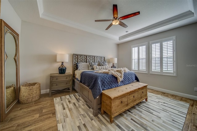 bedroom with ceiling fan, light hardwood / wood-style floors, crown molding, and a tray ceiling