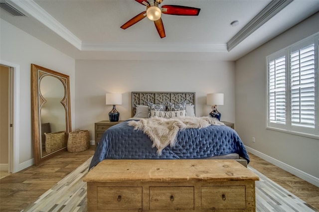 bedroom with ceiling fan, a tray ceiling, crown molding, and light hardwood / wood-style flooring