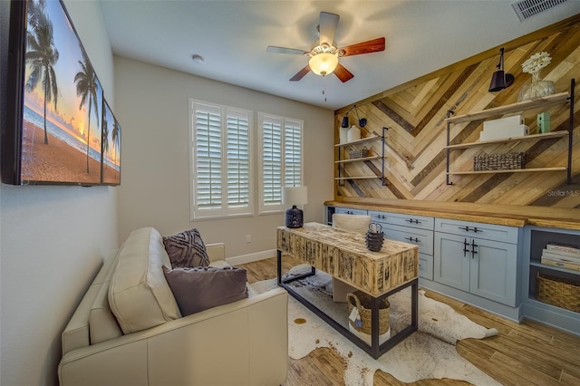 home office with light wood-type flooring, wood walls, and ceiling fan