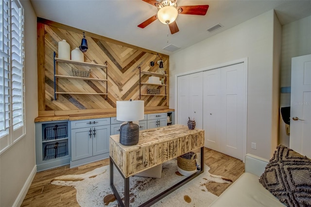 office area with light wood-type flooring, wood walls, and ceiling fan