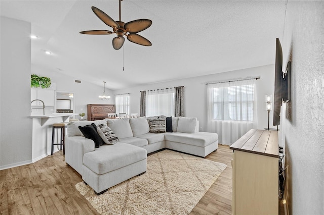 living room featuring light hardwood / wood-style floors, lofted ceiling, ceiling fan with notable chandelier, and a textured ceiling