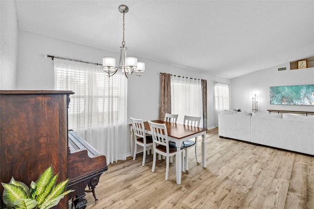 dining space featuring a chandelier, vaulted ceiling, and light hardwood / wood-style floors