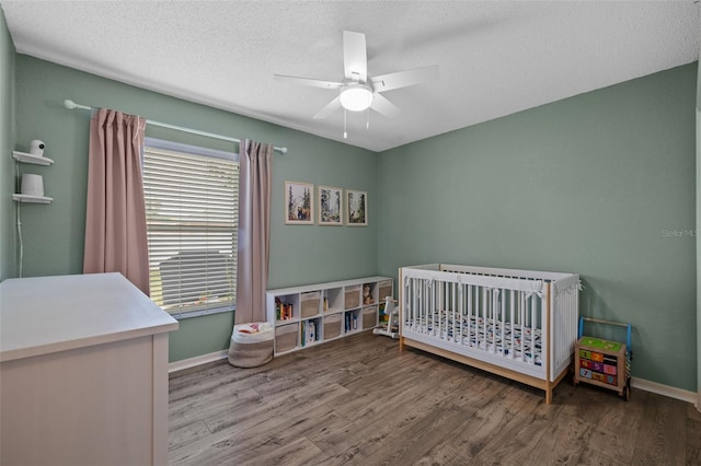 bedroom featuring a nursery area, hardwood / wood-style flooring, a textured ceiling, and ceiling fan