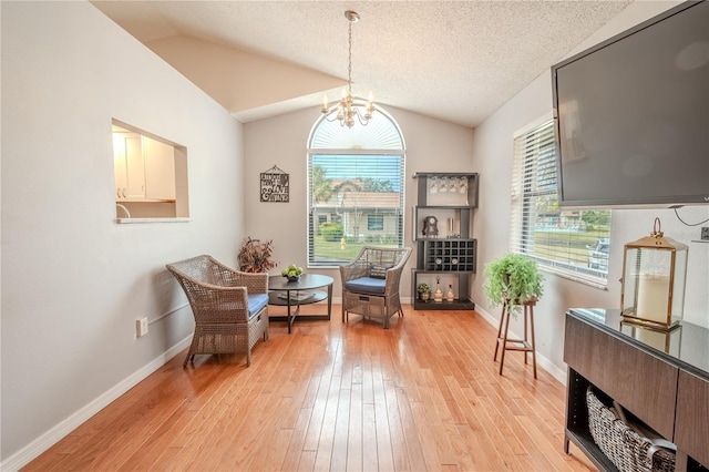 living area with a wealth of natural light, vaulted ceiling, light hardwood / wood-style floors, and a chandelier