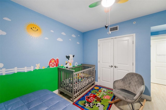 bedroom with hardwood / wood-style flooring, a crib, a closet, and ceiling fan