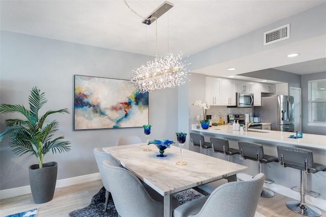 dining space with sink, an inviting chandelier, and light wood-type flooring