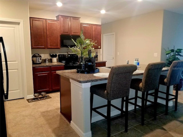 kitchen with a kitchen bar, light tile patterned flooring, black range with electric cooktop, and a kitchen island