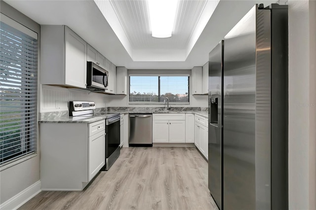 kitchen with stainless steel appliances, a raised ceiling, light wood-type flooring, white cabinetry, and dark stone countertops