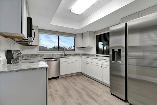 kitchen with stainless steel appliances, light stone countertops, a tray ceiling, sink, and white cabinetry