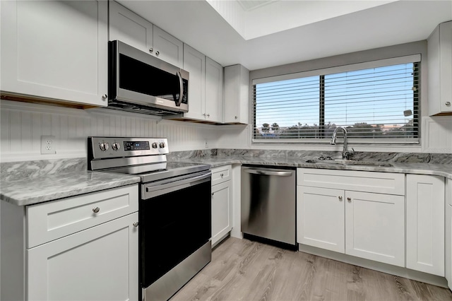 kitchen featuring appliances with stainless steel finishes, white cabinets, light stone countertops, and sink