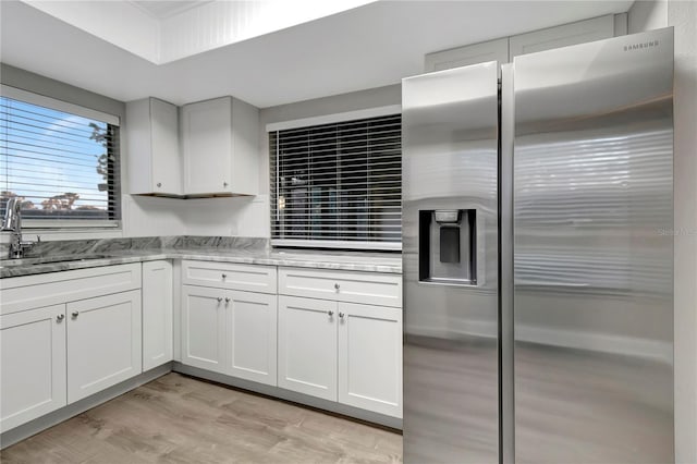 kitchen with white cabinets, light hardwood / wood-style floors, light stone countertops, stainless steel refrigerator with ice dispenser, and sink