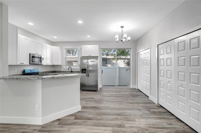 kitchen with kitchen peninsula, white cabinetry, light stone countertops, appliances with stainless steel finishes, and plenty of natural light