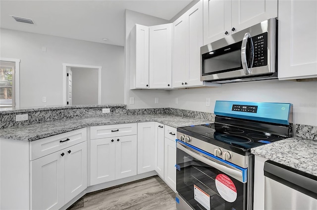 kitchen with light hardwood / wood-style floors, light stone countertops, white cabinets, and stainless steel appliances