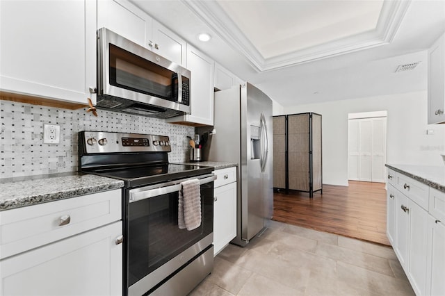 kitchen featuring light stone counters, white cabinetry, appliances with stainless steel finishes, and a tray ceiling