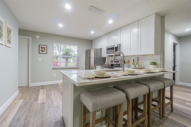 kitchen featuring a breakfast bar area, white cabinetry, light hardwood / wood-style floors, and appliances with stainless steel finishes