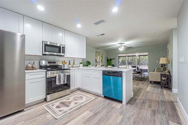 kitchen featuring light hardwood / wood-style floors, stainless steel appliances, kitchen peninsula, white cabinetry, and backsplash