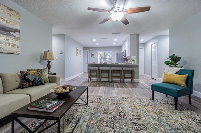 living room featuring sink, a textured ceiling, light wood-type flooring, and ceiling fan