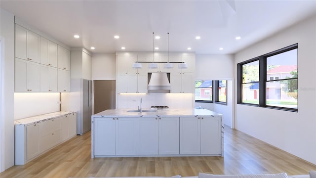 kitchen with white cabinetry, custom exhaust hood, stainless steel refrigerator, and an island with sink