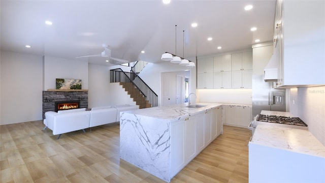 kitchen featuring white cabinetry, an island with sink, pendant lighting, light hardwood / wood-style flooring, and light stone counters