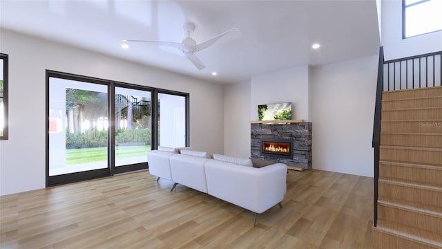 living room with ceiling fan, light wood-type flooring, and a stone fireplace