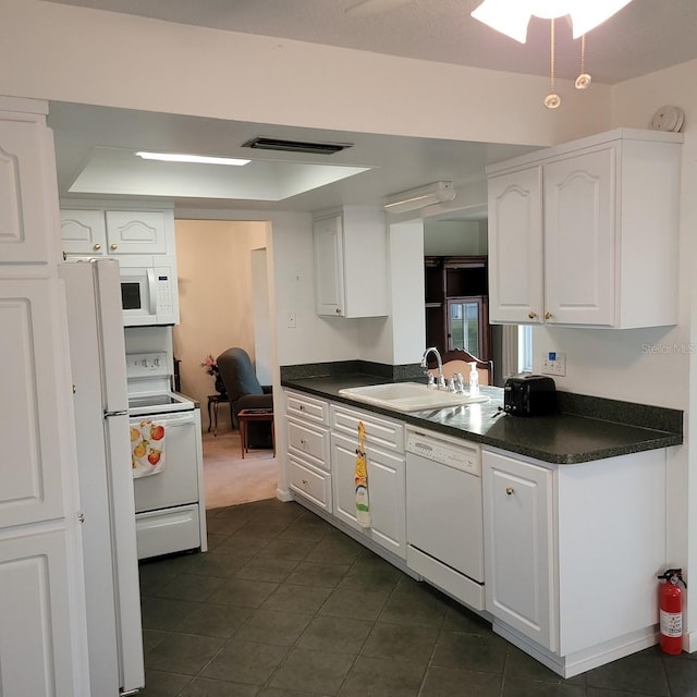 kitchen with dark tile patterned flooring, a raised ceiling, sink, white appliances, and white cabinetry