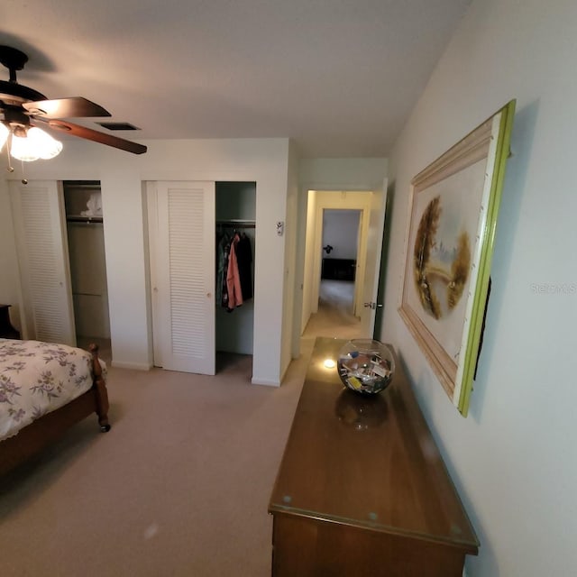 bedroom with ceiling fan, multiple closets, and light carpet