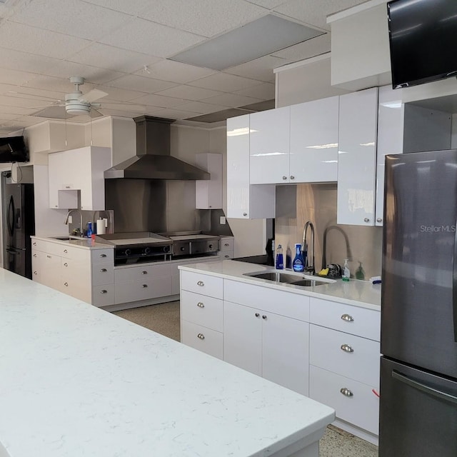 kitchen with wall chimney range hood, sink, white cabinetry, black refrigerator, and stainless steel fridge