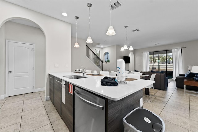 kitchen with sink, dishwasher, light tile patterned flooring, hanging light fixtures, and a center island with sink