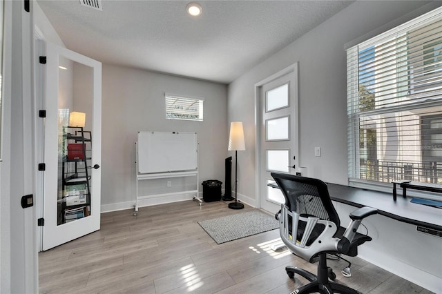 office area with light hardwood / wood-style floors, a textured ceiling, and plenty of natural light