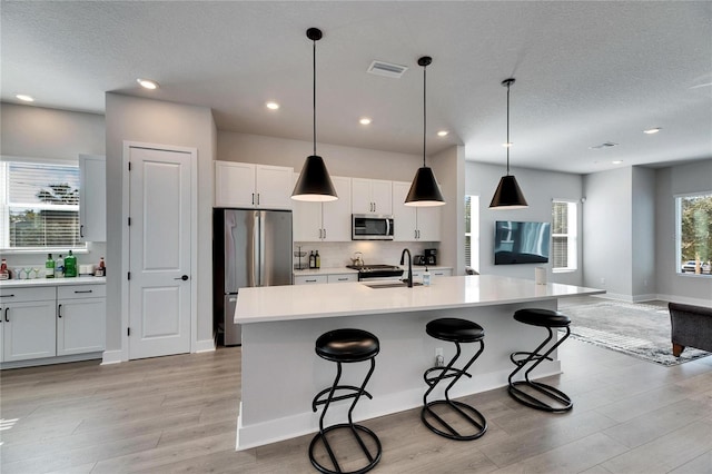 kitchen with sink, white cabinets, hanging light fixtures, a center island with sink, and appliances with stainless steel finishes