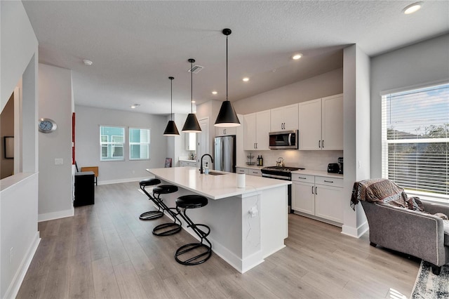 kitchen with appliances with stainless steel finishes, an island with sink, white cabinets, and a kitchen bar