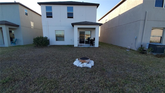 back of property with an outdoor fire pit, central air condition unit, and a lawn