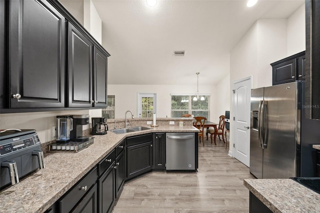 kitchen with vaulted ceiling, pendant lighting, sink, light hardwood / wood-style floors, and stainless steel appliances