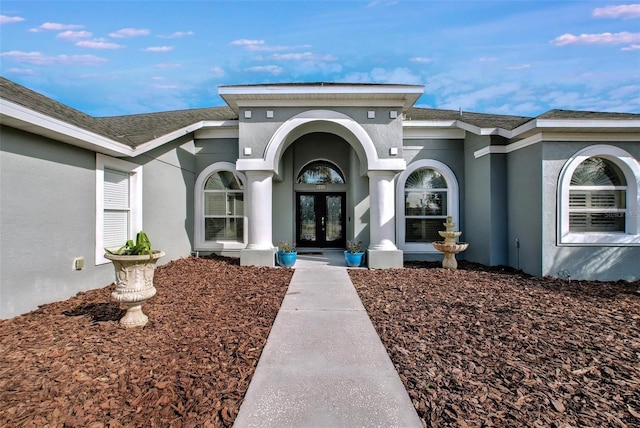 view of exterior entry featuring french doors, roof with shingles, and stucco siding