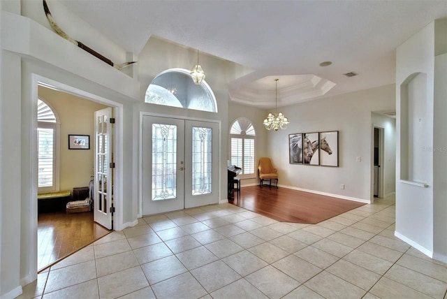 tiled entrance foyer with a chandelier, a tray ceiling, and french doors