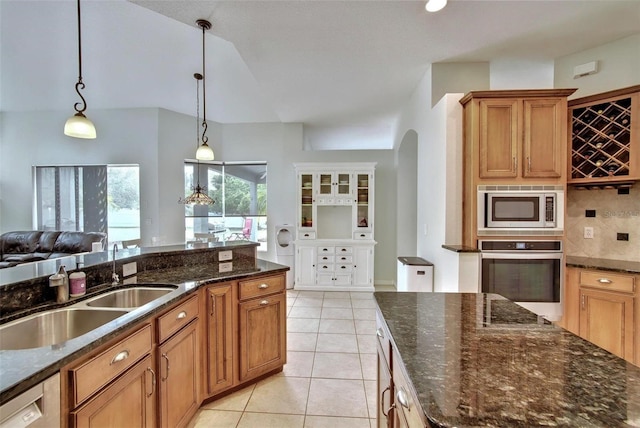 kitchen with sink, hanging light fixtures, appliances with stainless steel finishes, light tile patterned floors, and dark stone counters