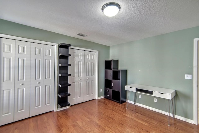 unfurnished bedroom featuring light hardwood / wood-style floors, two closets, and a textured ceiling