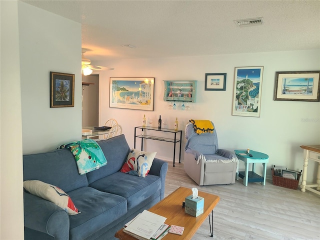 living room featuring a textured ceiling, light wood-type flooring, and ceiling fan