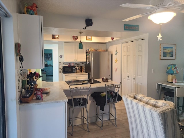 kitchen featuring kitchen peninsula, decorative light fixtures, black appliances, backsplash, and white cabinets