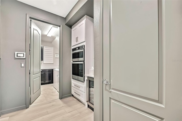 kitchen featuring white cabinetry, light wood-type flooring, stainless steel double oven, and wine cooler