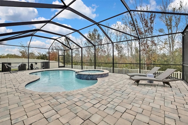 view of pool with a patio, glass enclosure, and an in ground hot tub