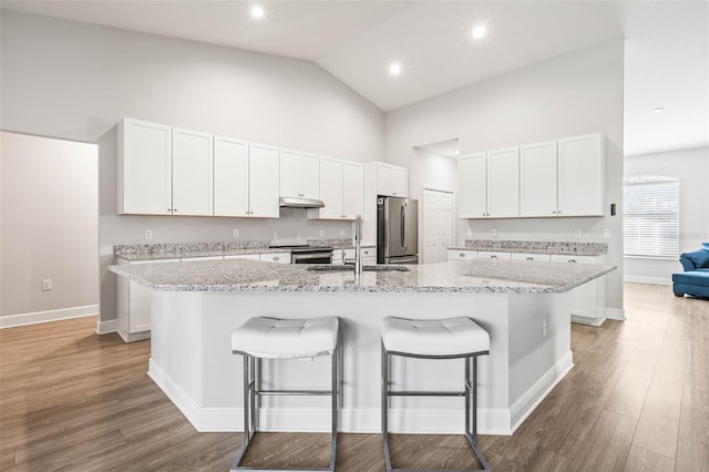 kitchen with a kitchen island with sink, appliances with stainless steel finishes, high vaulted ceiling, white cabinets, and light stone counters