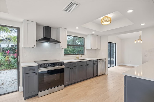 kitchen with white cabinetry, stainless steel appliances, hanging light fixtures, wall chimney exhaust hood, and sink