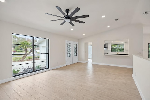 unfurnished living room featuring ceiling fan, vaulted ceiling, light wood-type flooring, and a healthy amount of sunlight